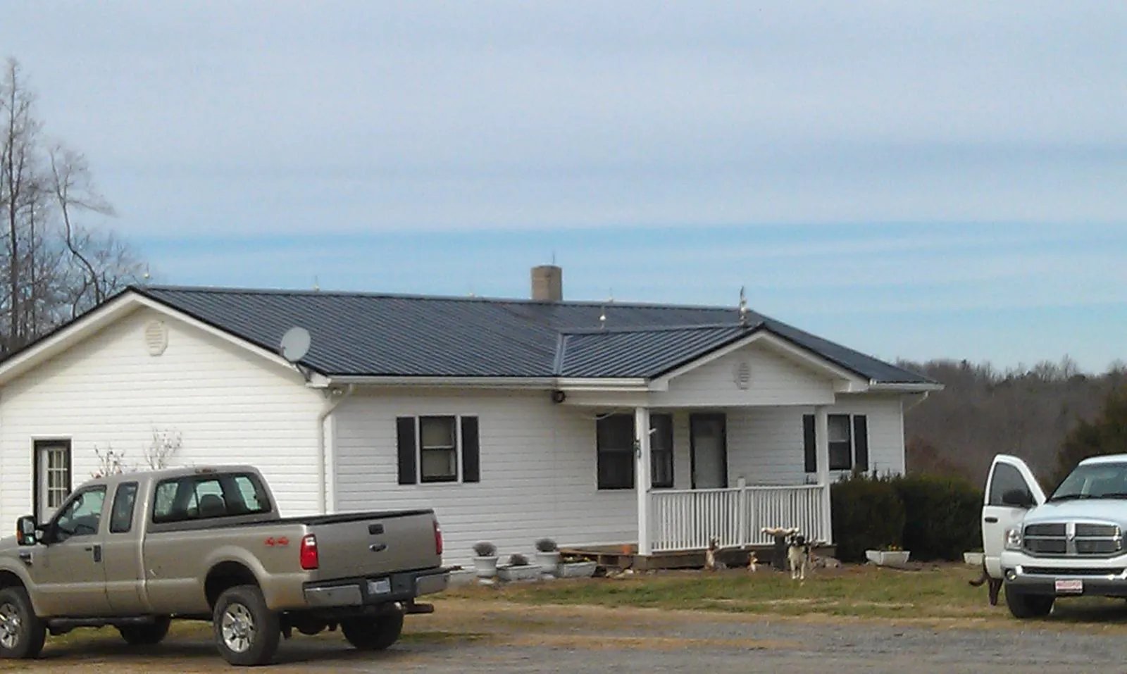 Finished dark metal roof on a white ranch home with work trucks parked in Milton